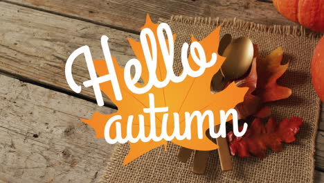 animation of hello autumn text over cutlery and autumn leaves over wooden background