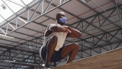 african american man jumping on box wearing face mask at gym