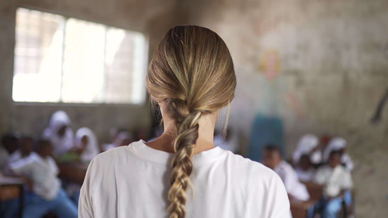 알 수 없는 백인 백인 금발 소녀가 어린 아이들과 함께 아프리카 학교에서 자원봉사자로 가르치고 있습니다.