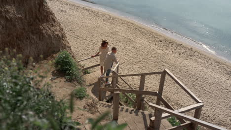 una pareja despreocupada de turistas de pie en una escalera de madera en una mañana soleada en la costa vacía.