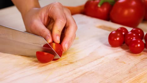 a hand slices cherry tomatoes with a knife