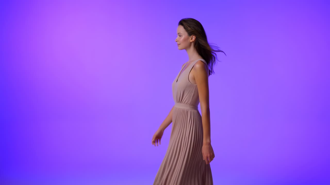 Jovem mulher caminhando graciosamente com um vestido plissado contra um plano de fundo roxo