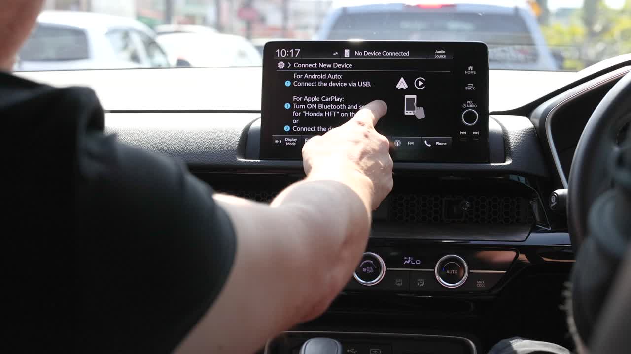 A driver operates a car's touchscreen console in daylight, adjusting settings and navigating menus in a parked vehicle