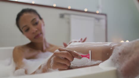 mujer de raza mixta tomando un baño afeitando sus piernas