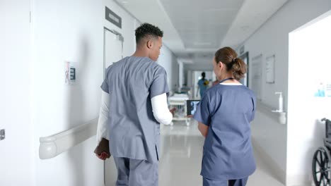 diverse doctors talking and using tablet in hospital corridor, slow motion