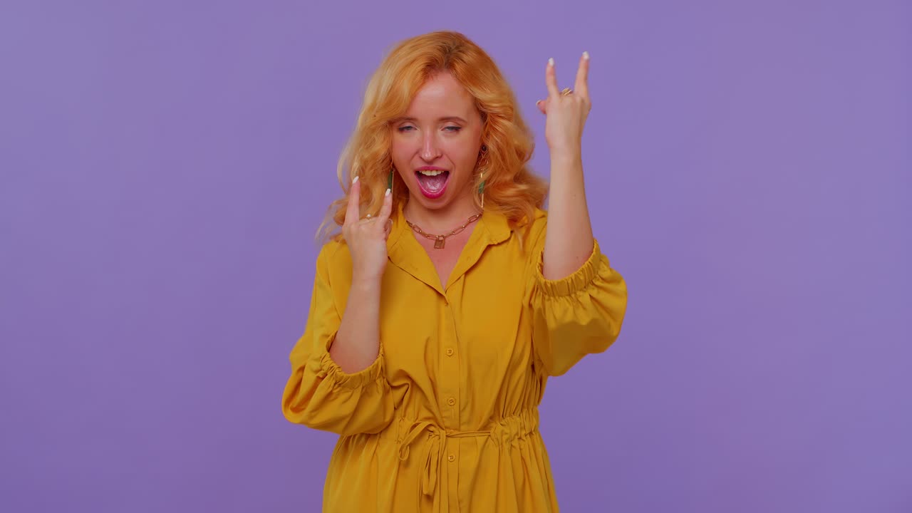Nadšená zrzavá dívka ukazuje rukama gesto „rock n roll“, křičí „jo“ s bláznivým výrazem.