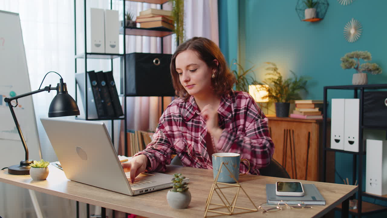 노트북 컴퓨터에서 일하는 사업가 여성이 뜨거운 커피 한 잔을 마시며 집 사무실에서 테이블에 앉아 있습니다.