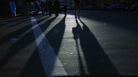 pedestrians pass in a crosswalk on a busy city street as long shadows stretch along the pavement