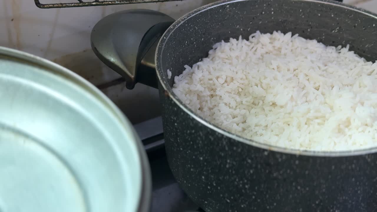 家庭のキッチン、コンロの上にある黒い調理鍋に入った炊きたての白米。手前には蓋があり、柔らかな室内照明が当たる。