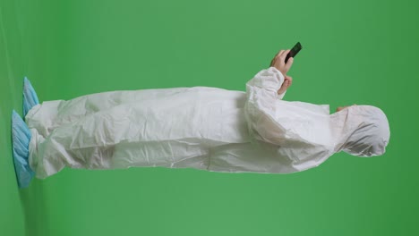 full body side view of asian male scientist using smartphone and look around while standing on green screen background