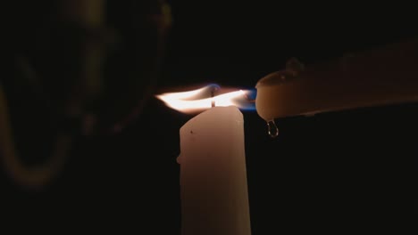 a lone white candle being lit by another candle that is dripping wax in slow motion