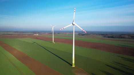 Drohnenaufnahme-Von-Rotierenden-Windkraftanlagen,-Die-An-Einem-Sonnigen-Tag-Auf-Einem-Landwirtschaftlichen-Feld-Installiert-Sind,-4k