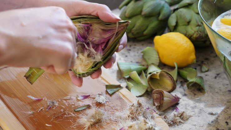 mujer limpiando el corazón de las alcachofas con cuchara. proceso de cocción en la cocina. listo para preparar