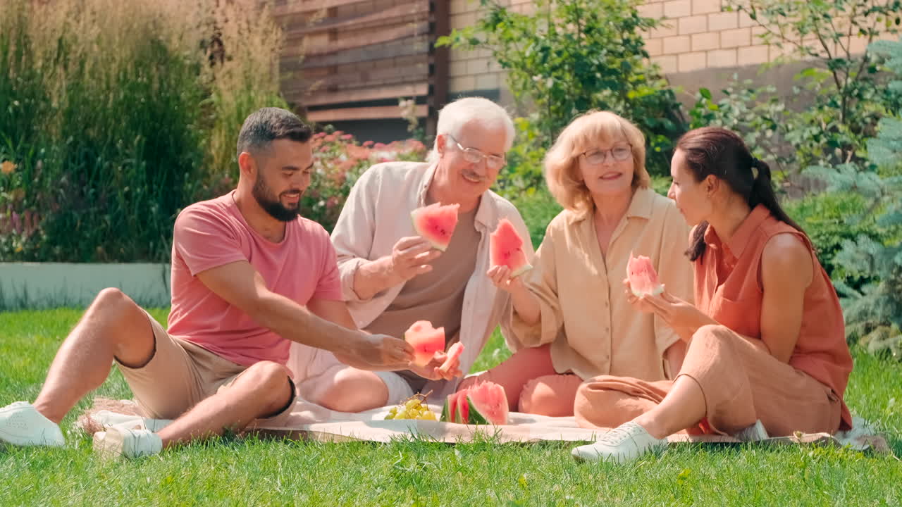 Multigenerational Couples Having Picnic In Backyard