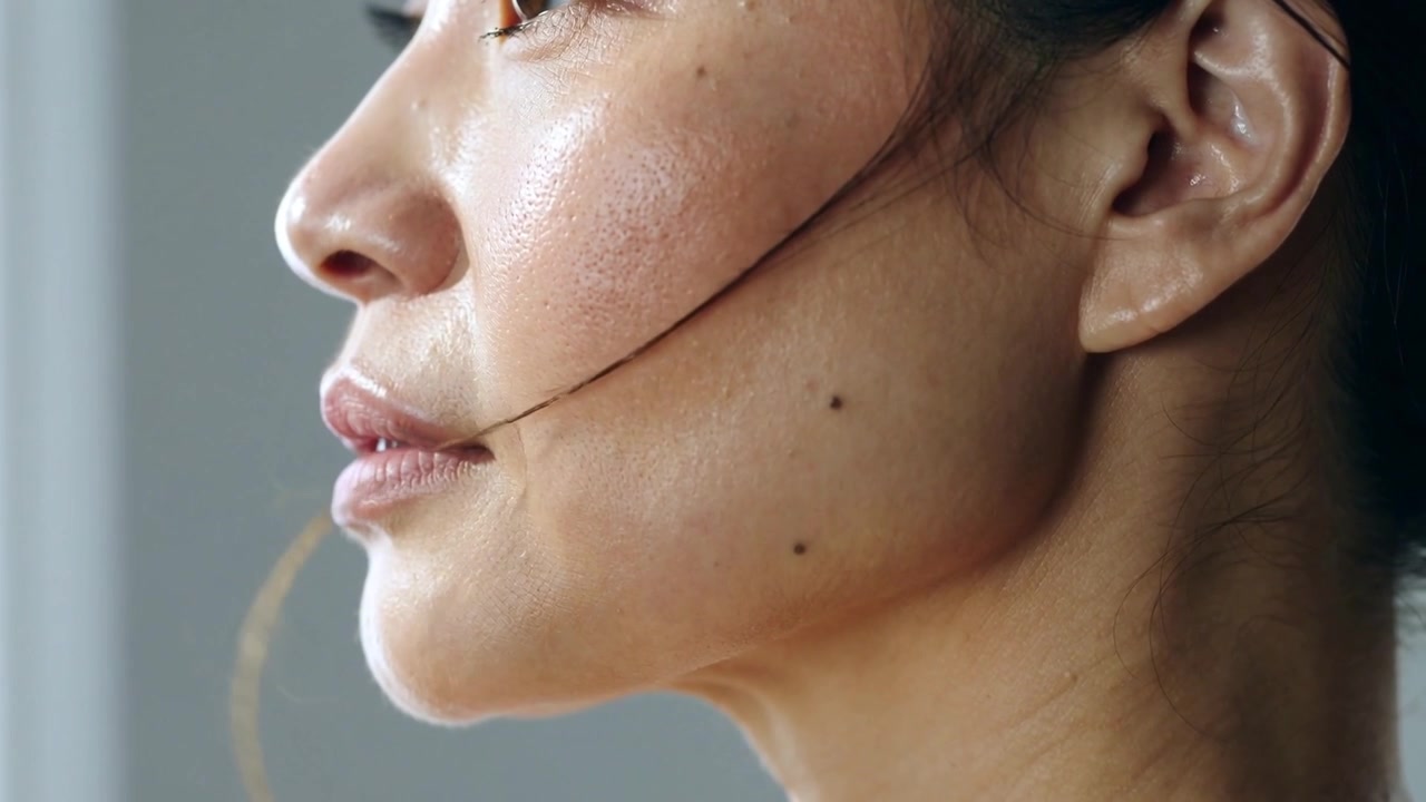 Mostrando una donna asiatica che rilassa la mascella, dischiudendo le labbra in primo piano mentre una ciocca di capelli le sfiora la guancia.