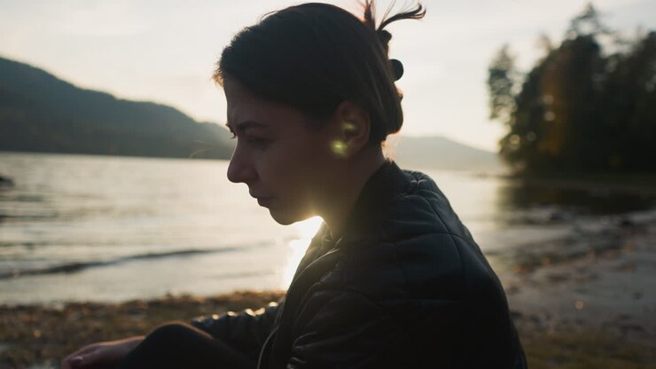Sad woman sitting on riverbank at sunset. Woman feels deep sadness worrying about loneliness. Calmness nature atmosphere to free negative emotions