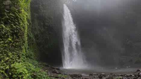 a big waterfall crashing down on big, black rocks in the jungle of bali, camera dolly shot from left to right