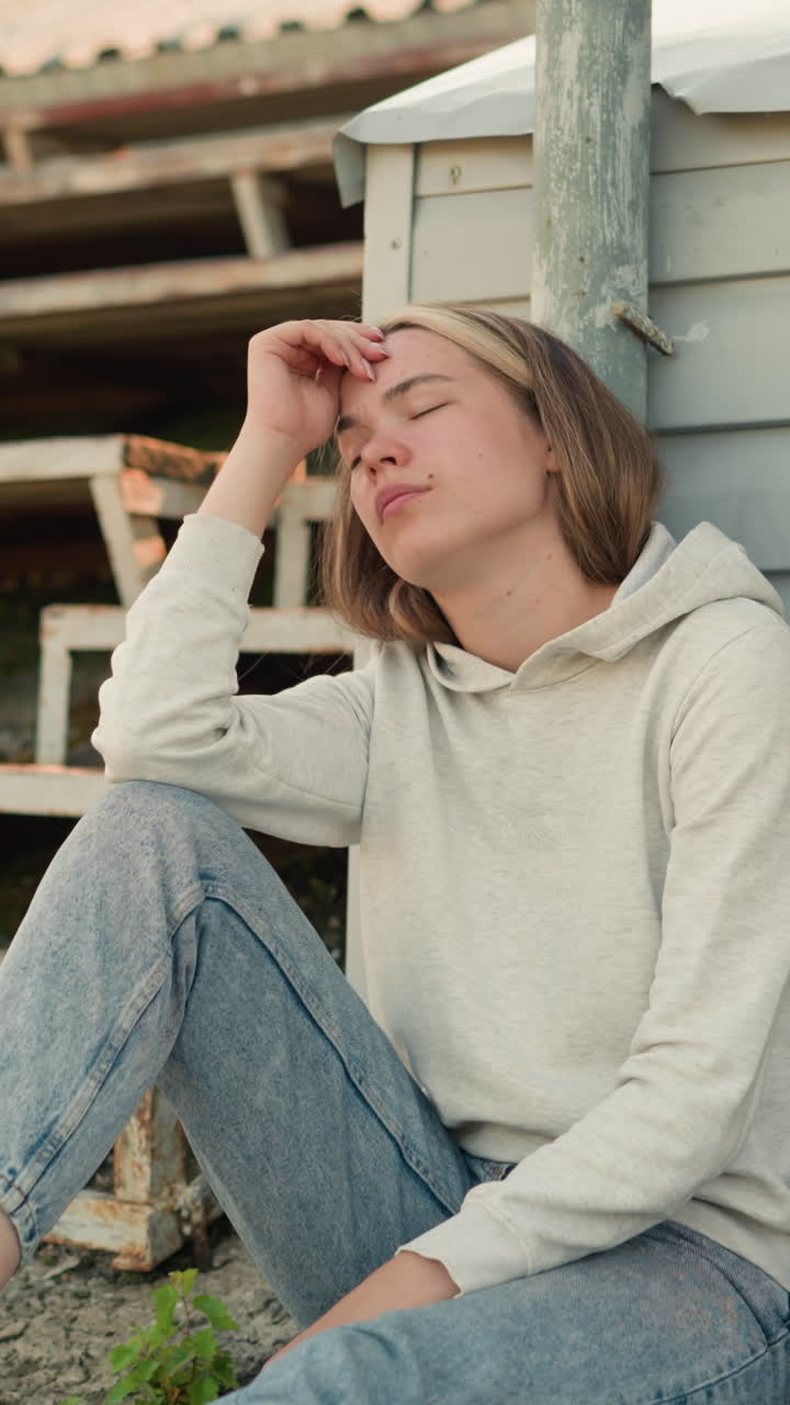 머리에 손을 은 청바지를 입은 여성, 그녀의 에 검은 가방이있는 경기장에서 앉아있는 동안 사려 깊은 반사를 표현합니다. 배경에는 은 관중석이 포함됩니다.