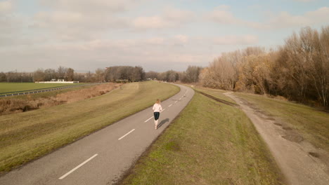 Vista-Aérea-De-Una-Mujer-Joven-Delgada-Corriendo-En-Un-Sendero-Con-árboles-De-Otoño-En-El-Fondo---Vídeo-De-Stock