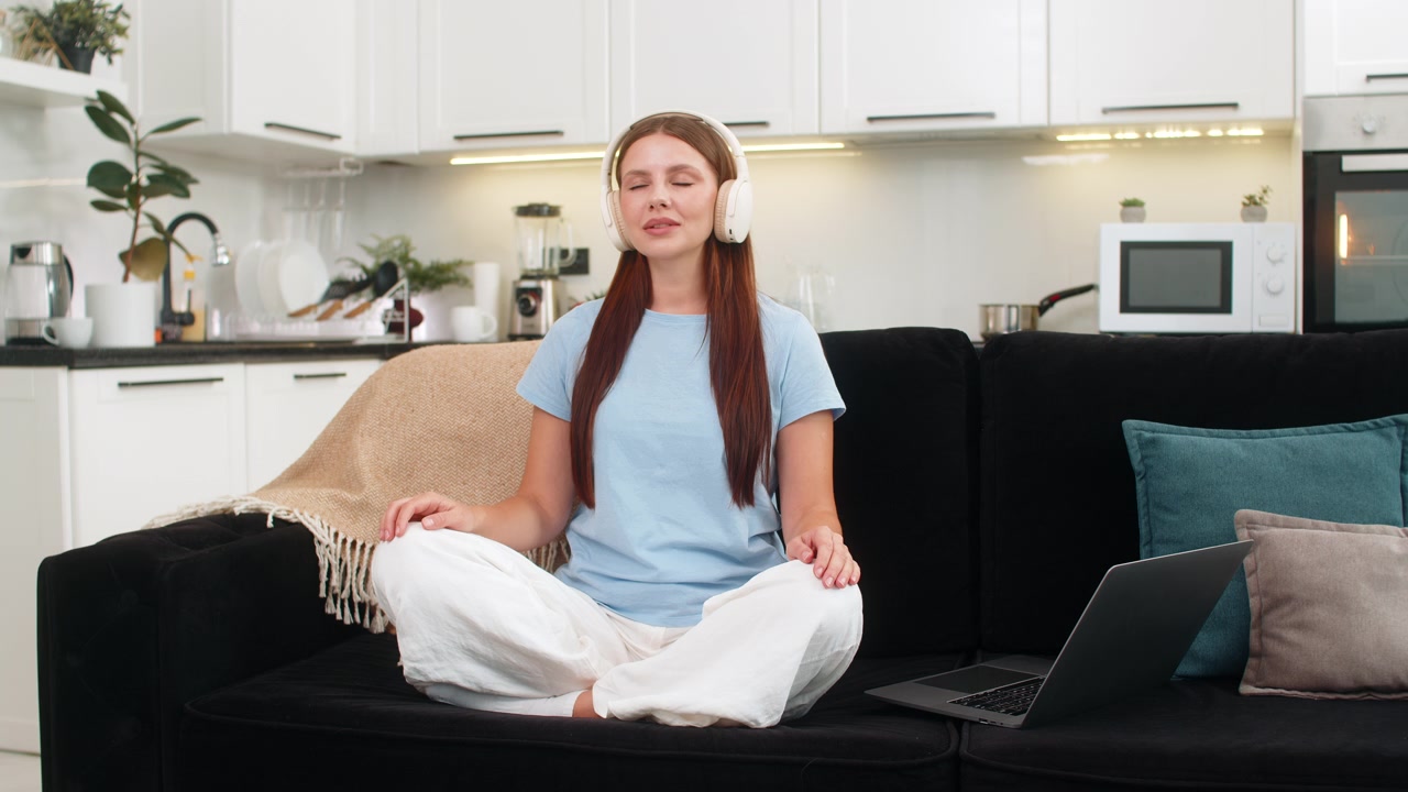 Young woman starts breathing practice on laptop with headphones closes eyes smile after session calm