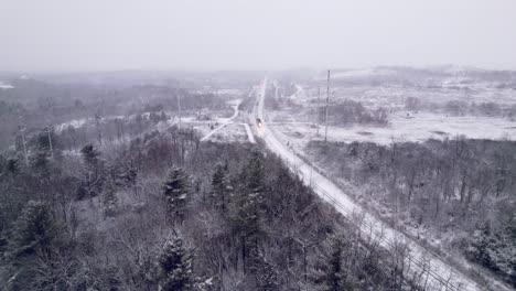 Commuter-Train-Approaches-during-a-Blizzard-in-a-Snow-Covered-Winter-Landscape,-Tracking-Aerial-Drone,-Ontario-Canada