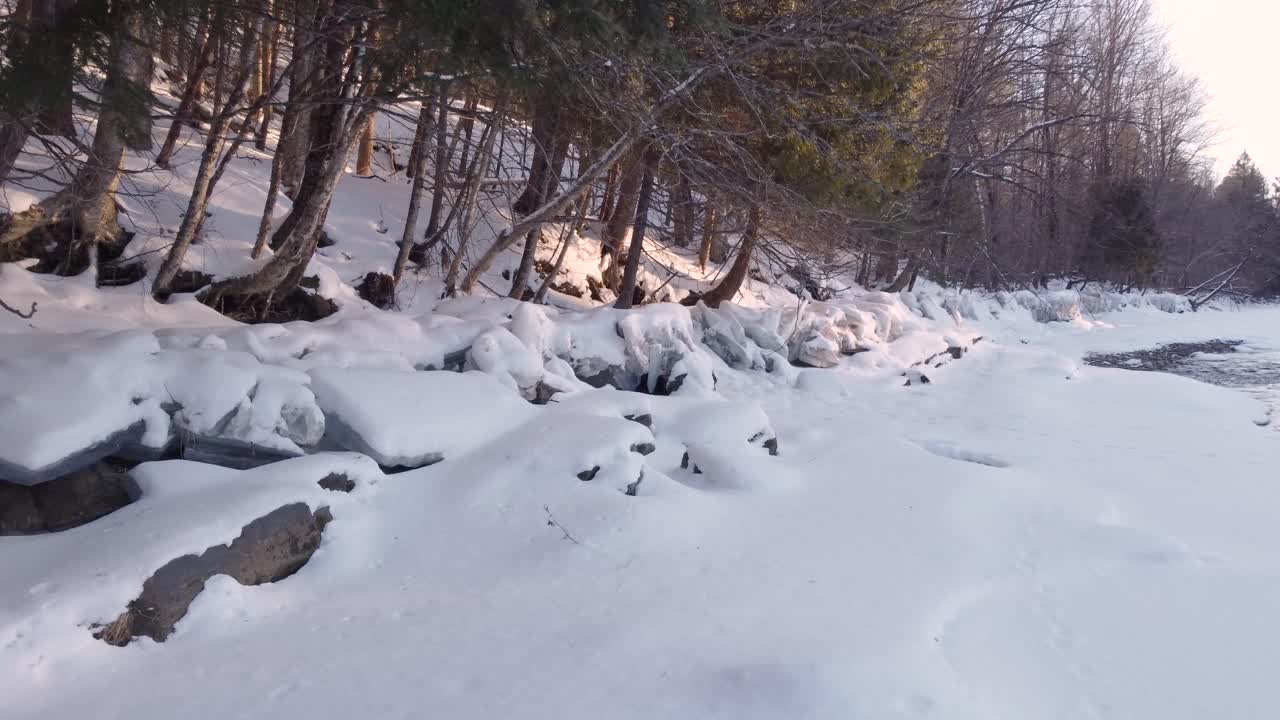 Snowy Landscape With Frozen Riverbank, Ice Formations, And Trees In Sherbrooke, Canada. drone shot