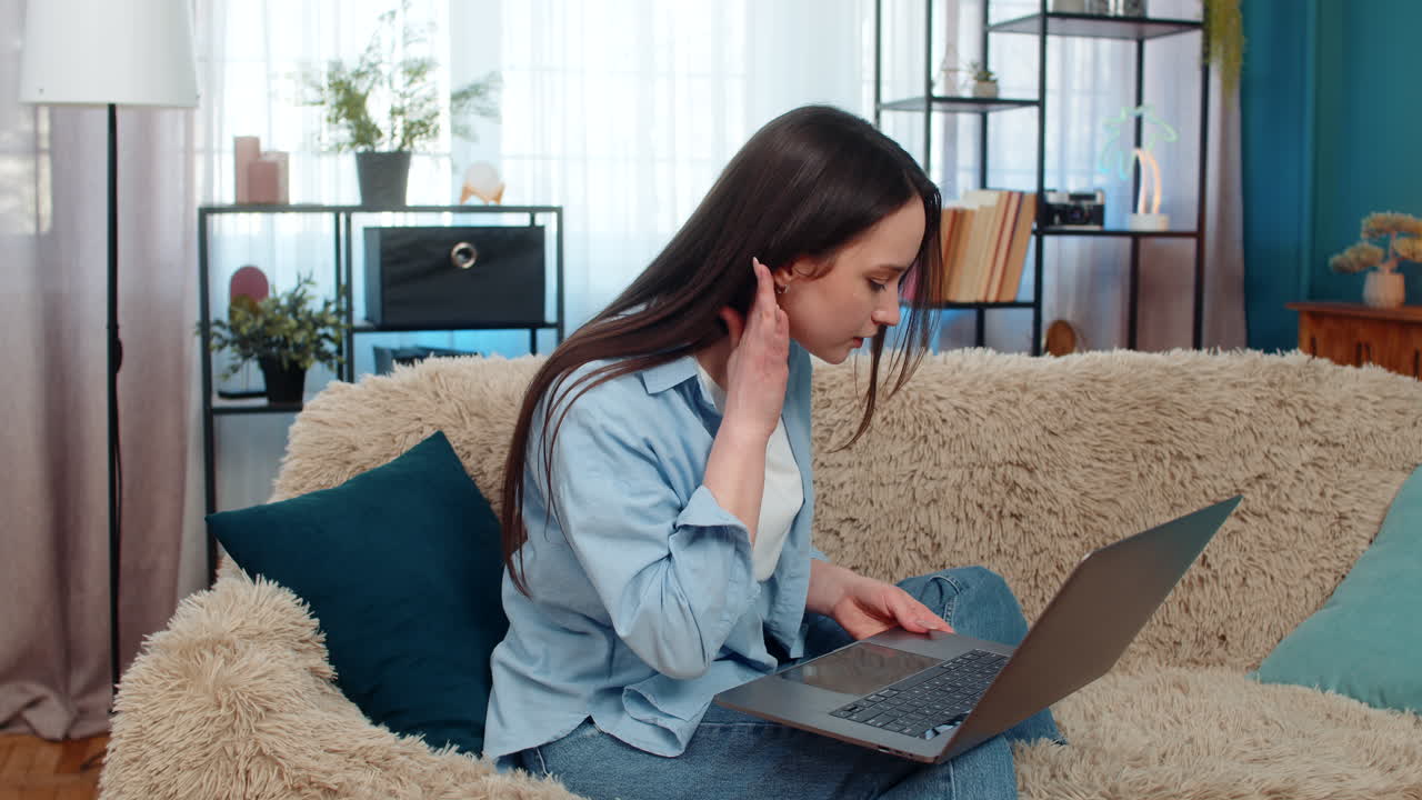 Young woman irritated sits on sofa arguing over laptop poor video call emotionally gesturing angry