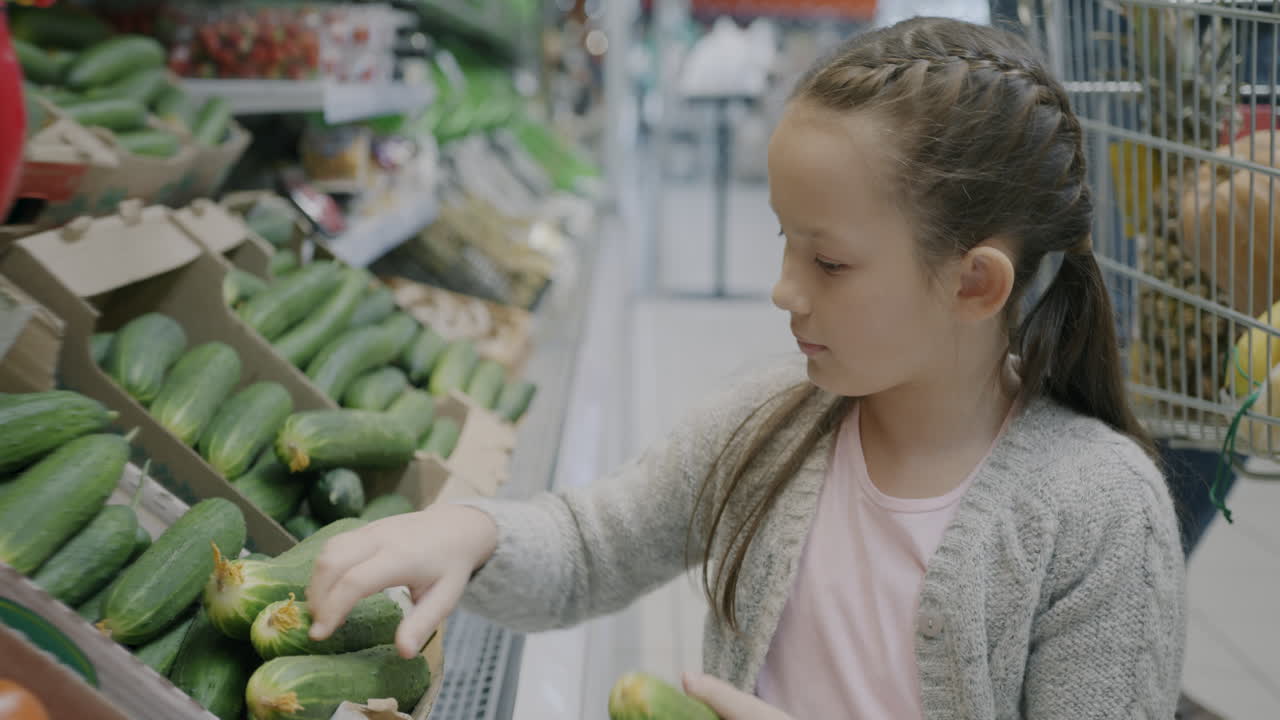 Young girl inspecting cucumbers in a grocery store