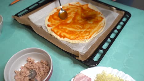 Spreading-tomato-on-pizza-dough-placed-on-baking-sheet