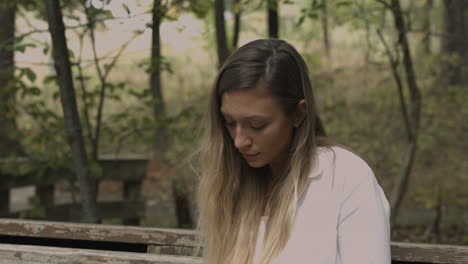 Still-portrait-young-blonde-woman-sitting-in-the-woods-looking-up-at-trees