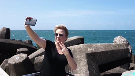 mujer joven tomando un selfie en el teléfono celular en el muelle con el océano al fondo