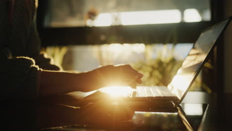 Hands-on-the-laptop-keyboard.-Silhouette-against-the-background-of-a-window-from-which-the-setting-sun-shines