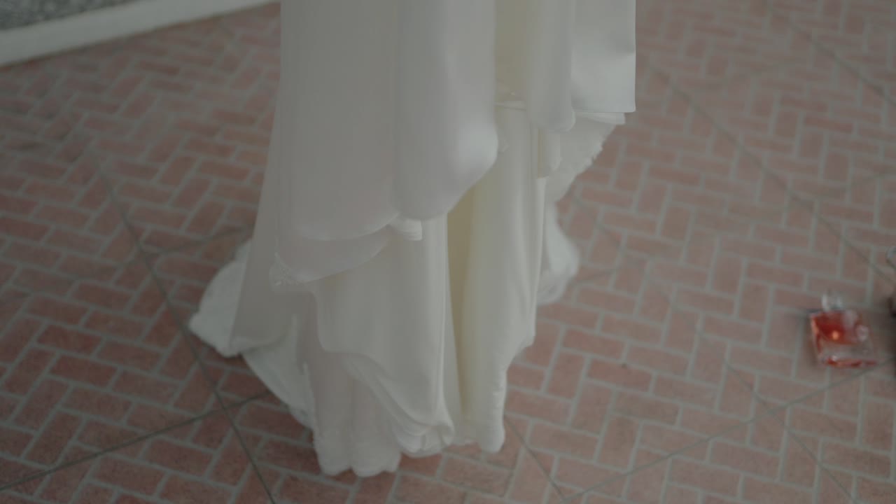 Close-up of a flowing white dress touching a textured brick floor with a soft, airy feel