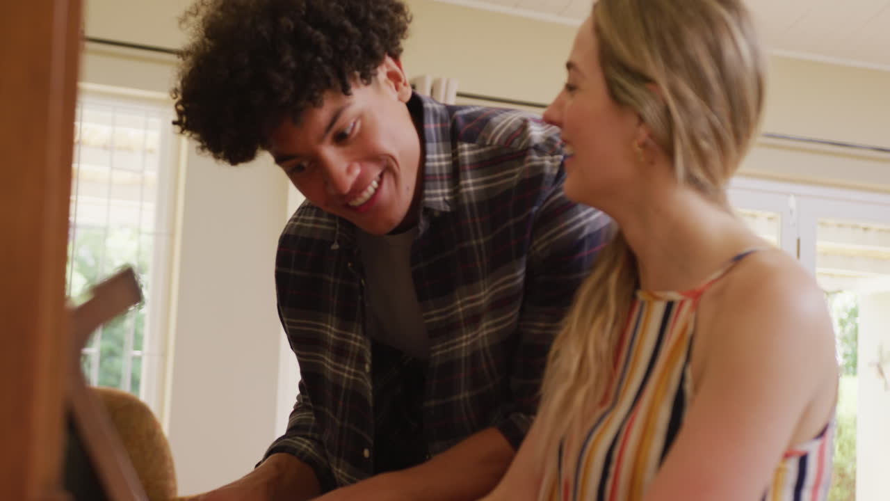una pareja feliz y diversa sonriendo y tocando el piano juntos en casa