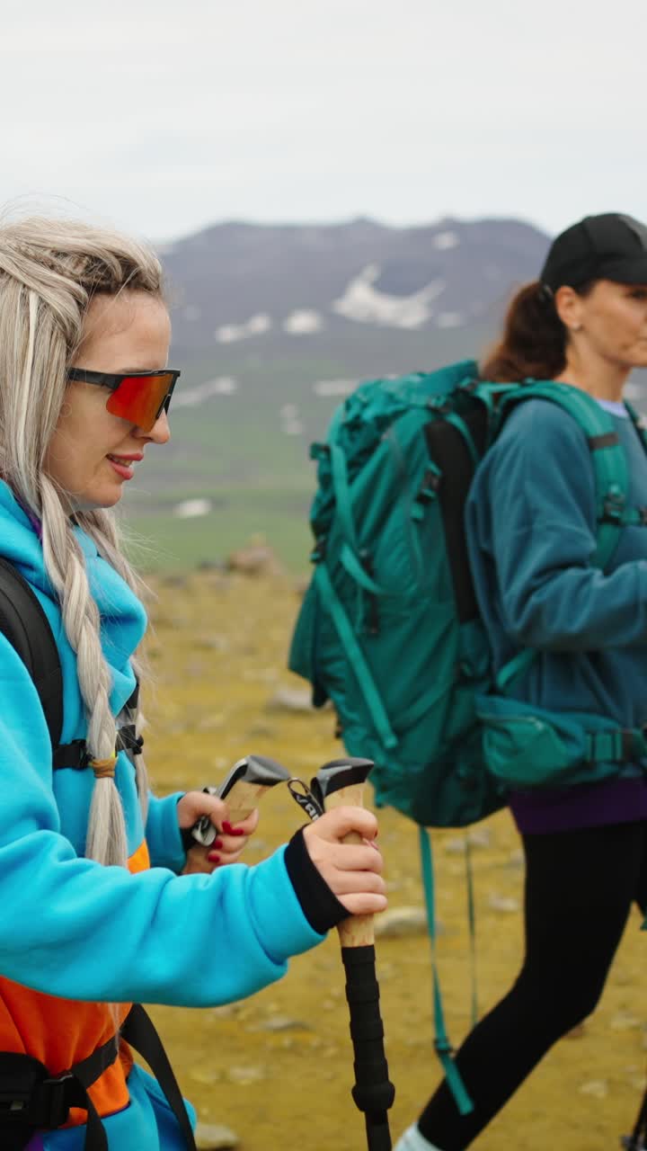 Due donne in escursione con zaini e bastoncini da trekking in un paesaggio montano.