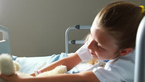 sick girl playing with teddy bear on bed