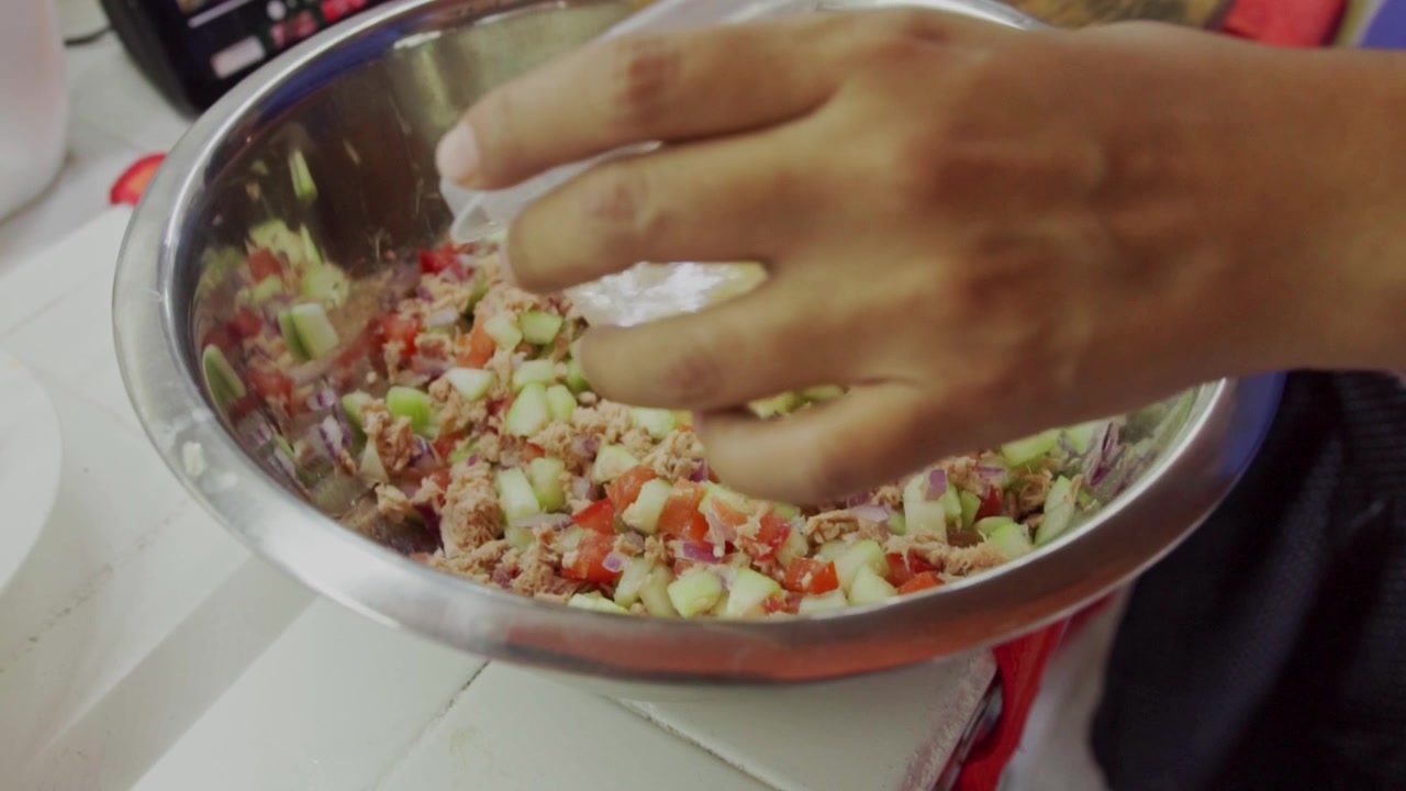 Primo piano ripreso a mano di mani che mescolano verdure tritate e tonno in una ciotola di metallo per il ceviche. Perfetto per tutorial di cucina o blog culinari.
