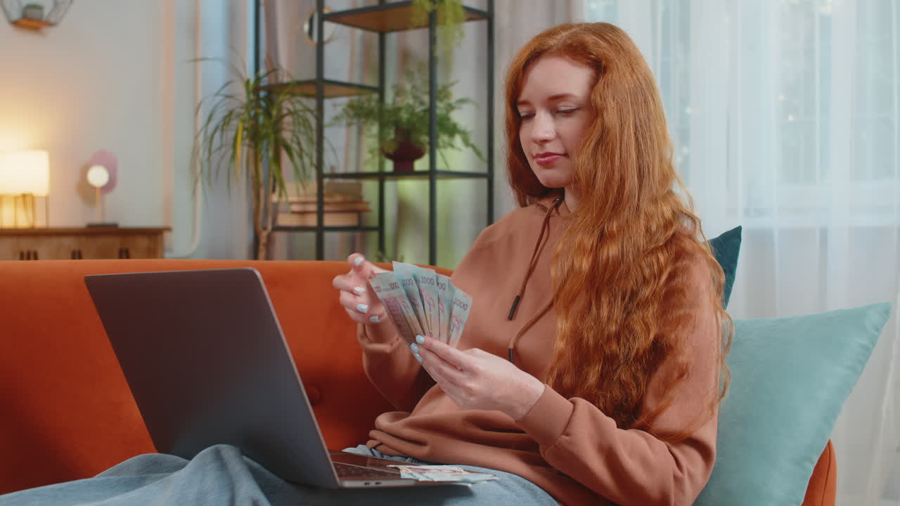 Rich happy woman counting money ukrainian hryvnias uah cash using laptop calculate domestic bills