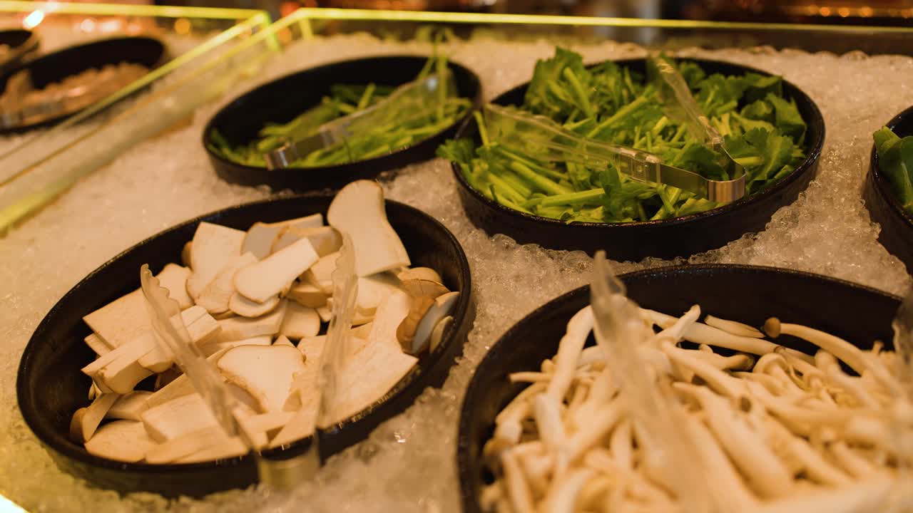 Camera pans across iced buffet bar with mushrooms, greens, corn, carrots under warm lighting