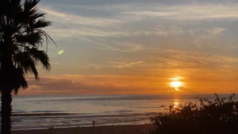 Unglaublich-Schöne-Sonnenuntergangsreflexionen,-Atlantikwellen-Am-Strand-Von-Carcavelos,-Orangefarbene-Blautöne,-Mann,-Der-In-Wasserwellen-Bei-Ebbe-Geht