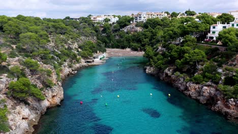 Cala-Pi-Beach-in-Mallorca-Spain-turquoise-inlet-with-buoys-and-bathers,-Aerial-lowering-approach-shot