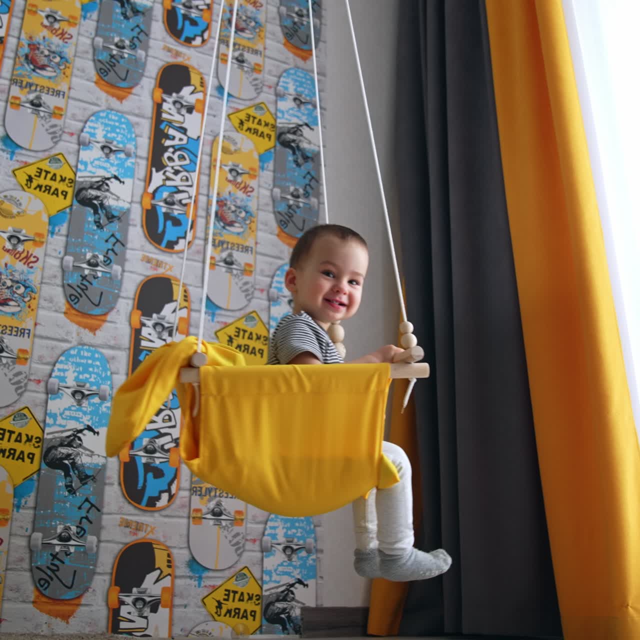 Smiling happy baby boy in a yellow swing. Adorable child waving his hand to the cat. Low angle view