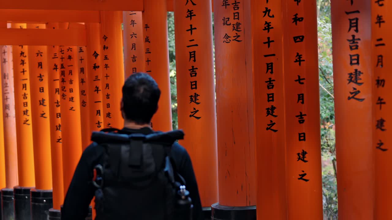 A traveler walks through the endless vermillion torii gates of Fushimi Inari Shrine in Kyoto, Japan.