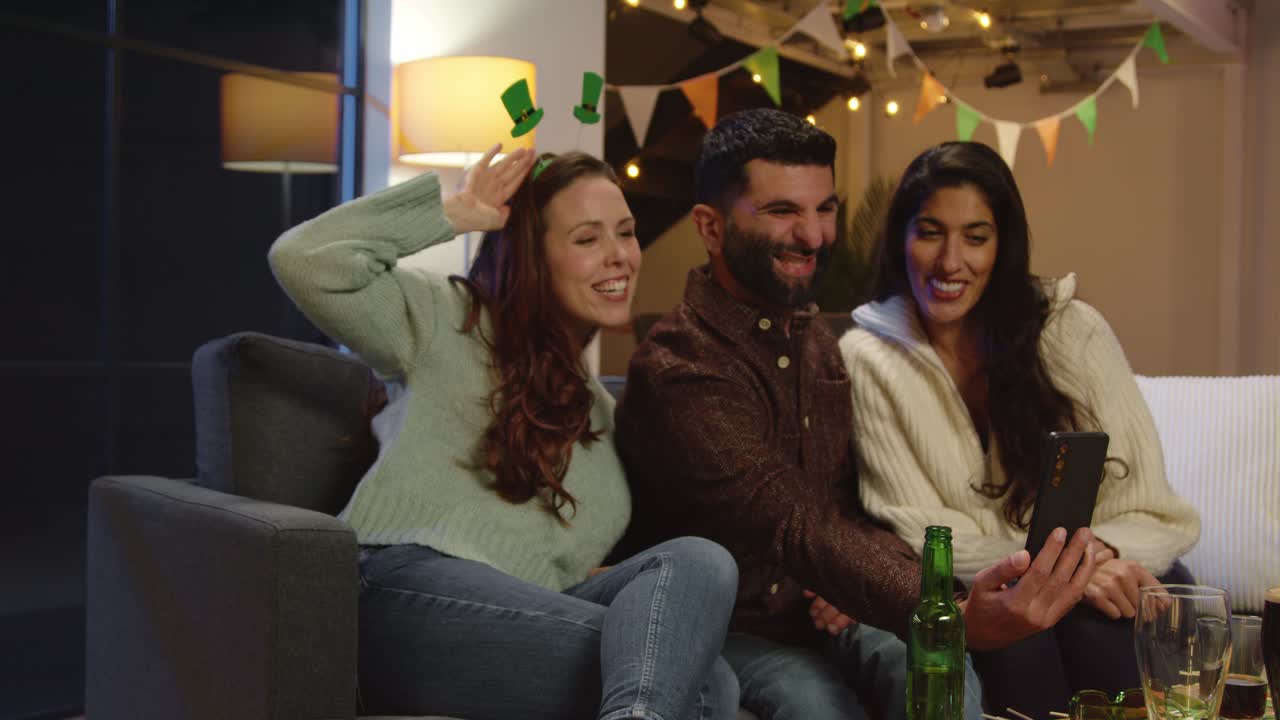 Group Of Friends Dressing Up At Home Or In Bar Celebrating At St Patrick's Day Party Posing For Selfie On Phone