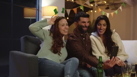 Group-Of-Friends-Dressing-Up-At-Home-Or-In-Bar-Celebrating-At-St-Patrick's-Day-Party-Posing-For-Selfie-On-Phone