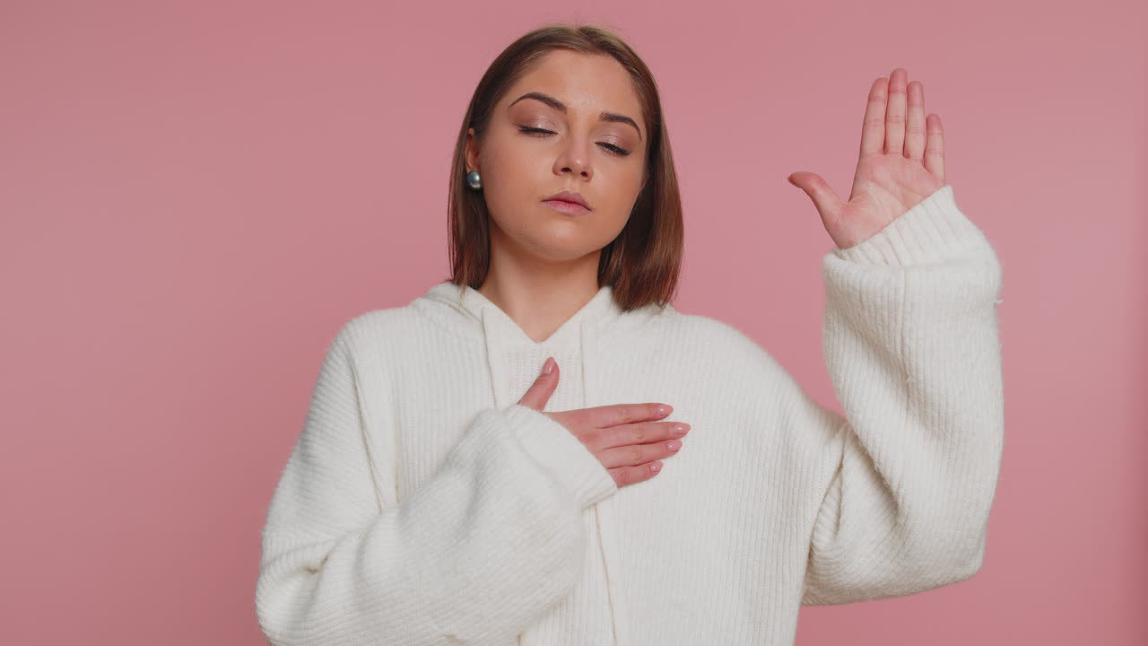 색 스웨터를 입은 젊은 여성이 분홍색 배경 앞에 서 있습니다.