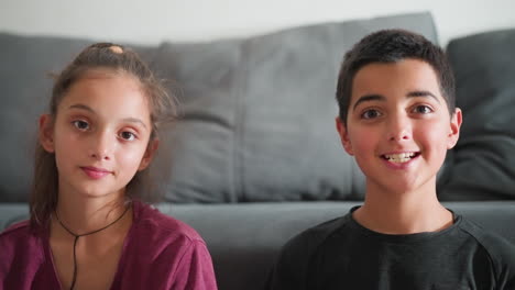 portrait view of beautiful kids sitting indoors looking directly at camera with soft expressions while boy slightly smiles and girl maintains calm face both appearing composed against cozy background