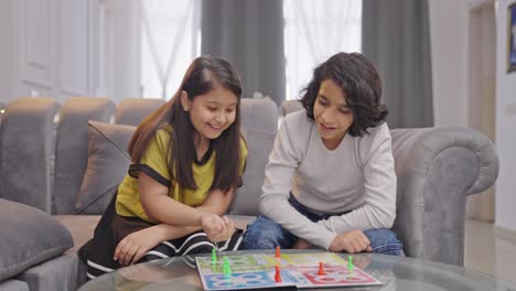 happy indian siblings playing ludo board game with dice