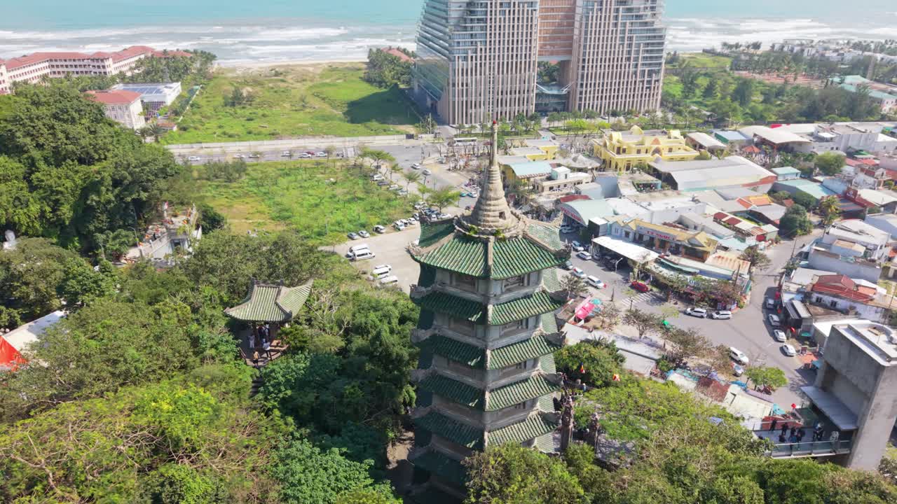 Quang cảnh từ trên cao của chùa bên bờ biển, nằm cạnh sự phát triển đô thị, các bãi đỗ xe và khách sạn cao tầng. Bãi biển và đường bờ biển hiện rõ ở đường chân trời, tạo nên một khung cảnh ban ngày sống động.