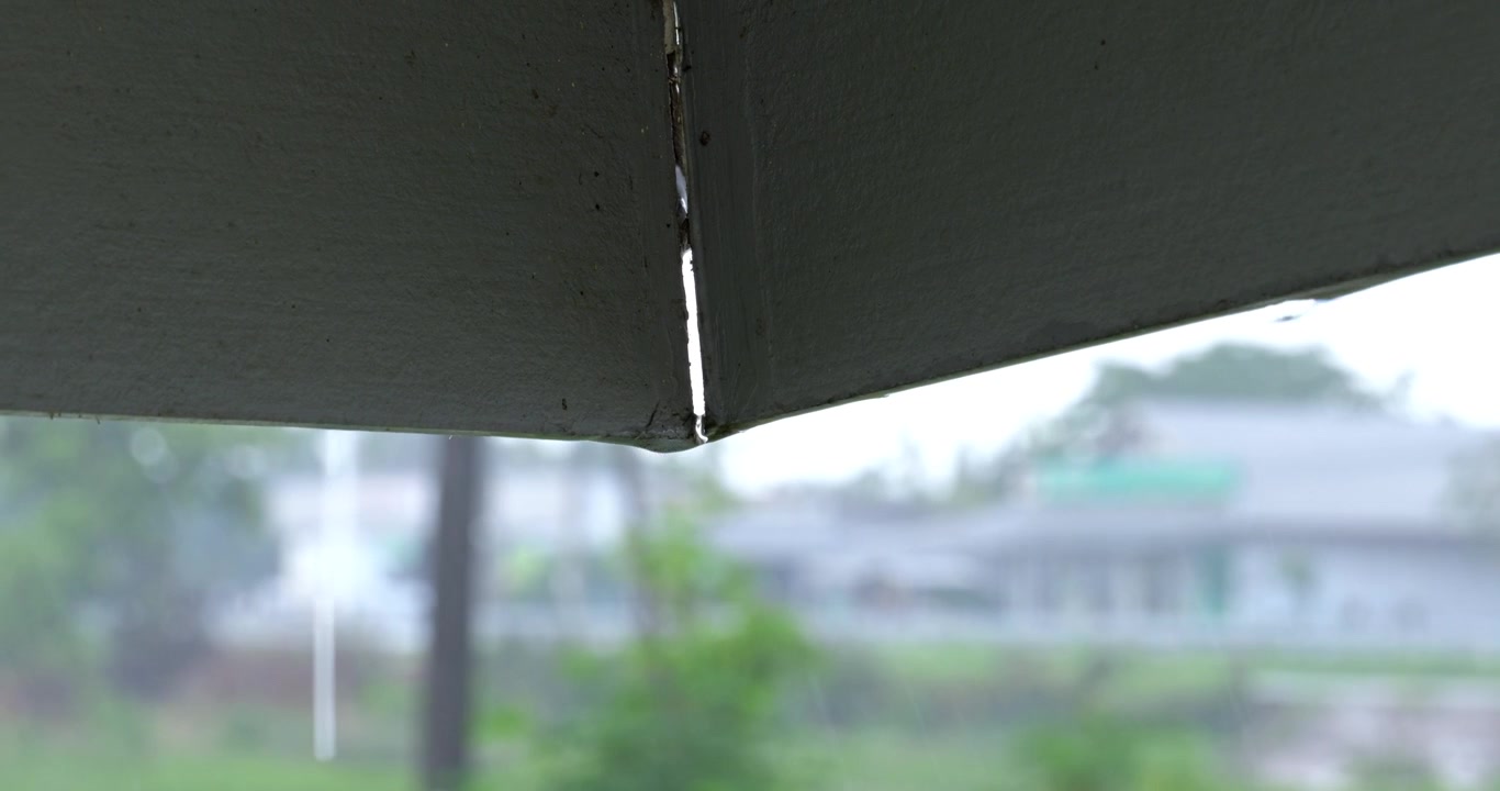 A serene and moody indoor view of rain pouring outside, seen through partially closed window blinds. Highlighting the cozy domestic atmosphere, tranquility, and relaxing atmospheric weather.